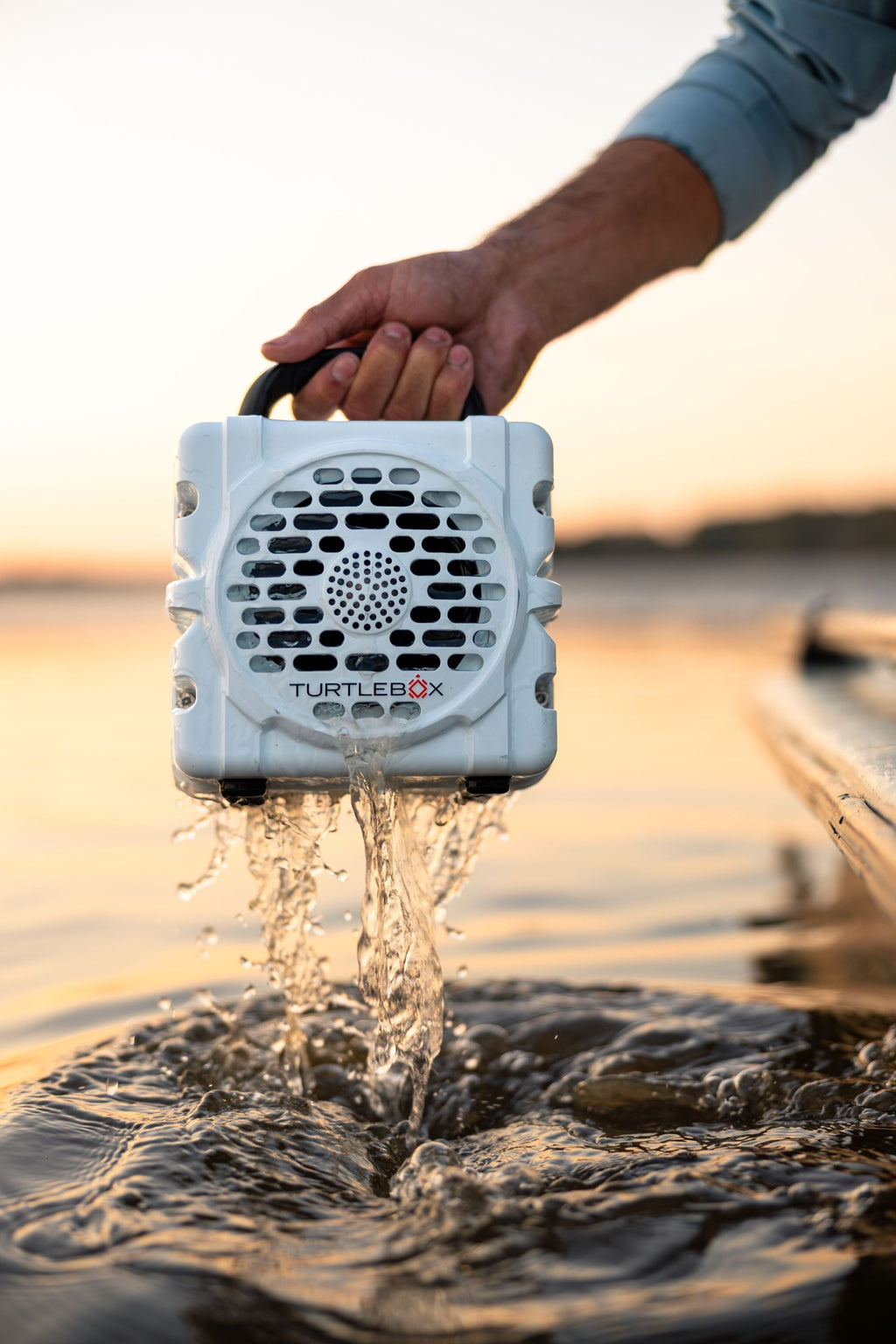Turtle Beach speaker being held above water with a sunset background #base-color_white