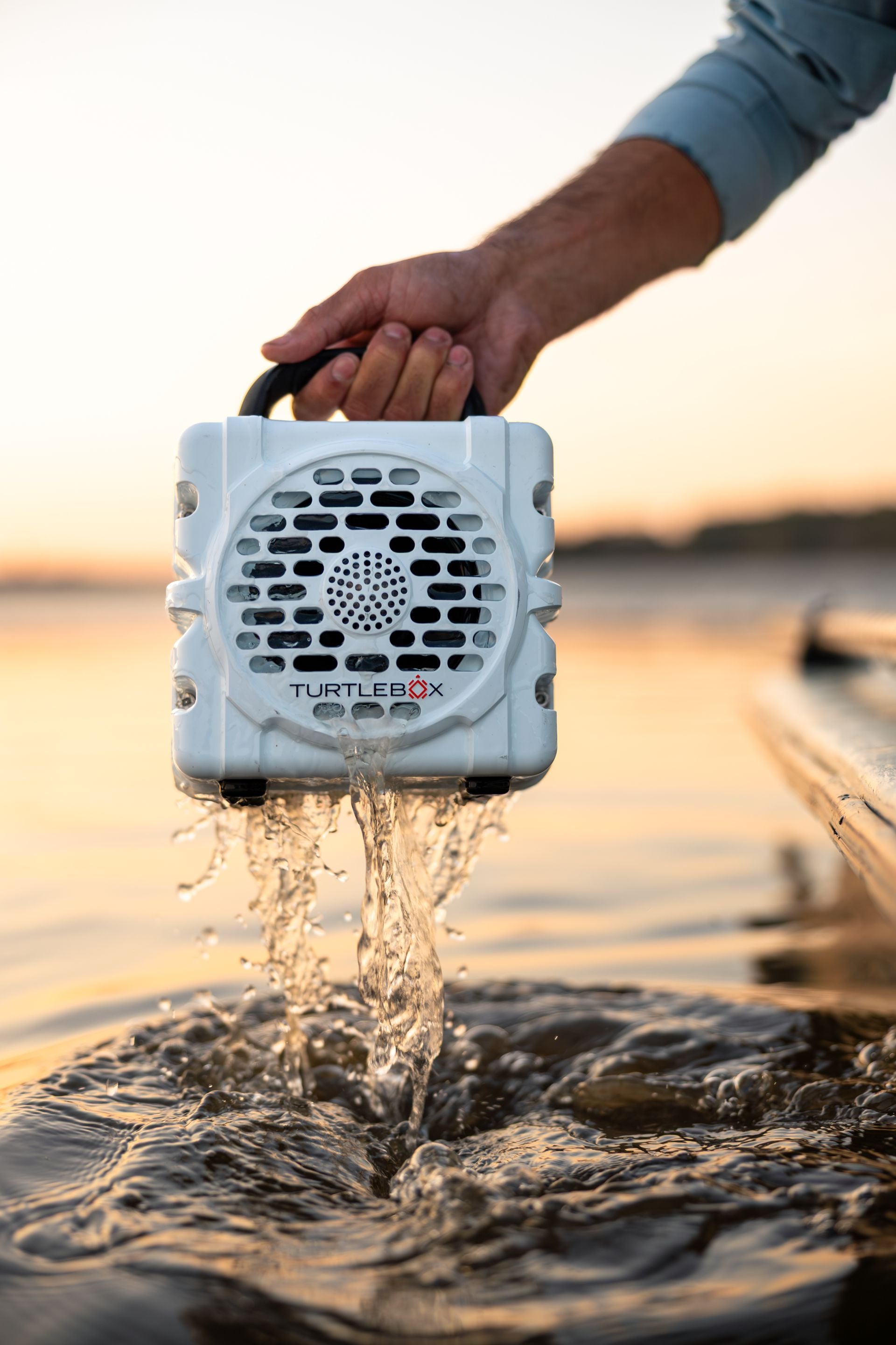 Turtle Beach speaker being held above water with a sunset background #base-color_white